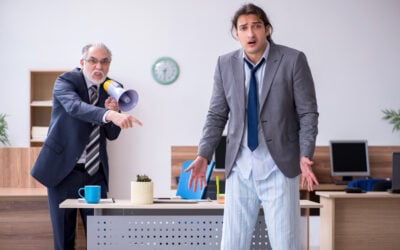 Employee sitting silently while an angry supervisor publicly criticizes the employee during a workplace meeting, illustrating the difference between workplace bullying and unlawful discrimination.